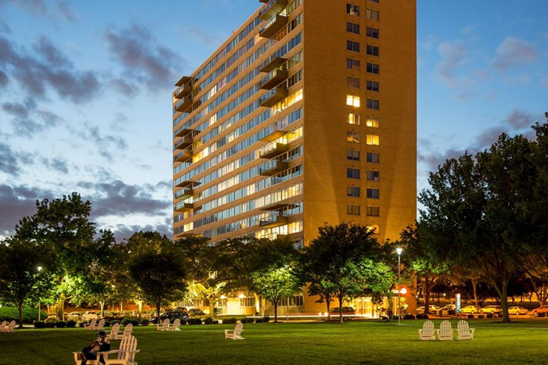 A large building with trees and lawn chairs in front of it.