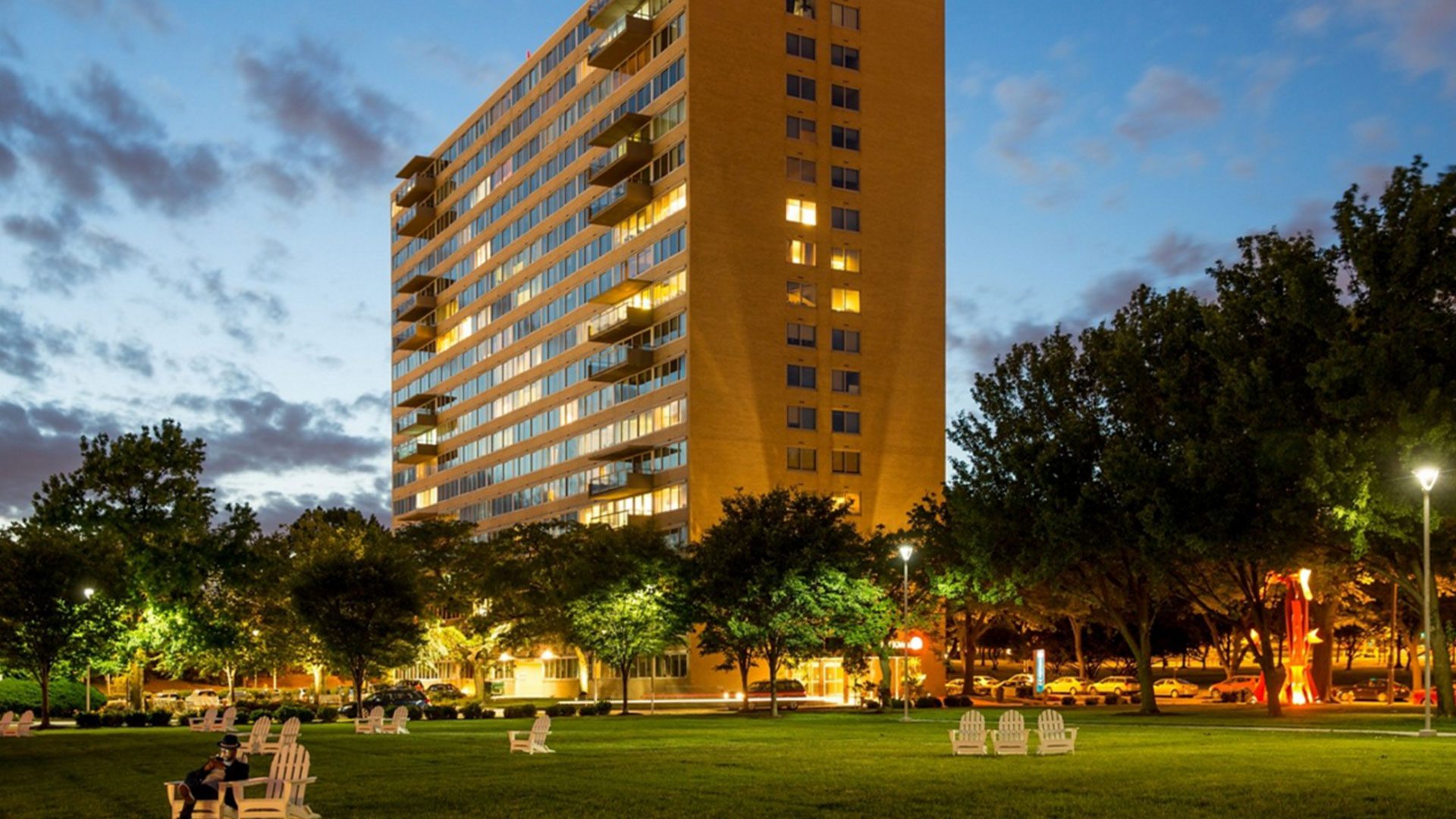 A large building with trees and lawn chairs in the foreground.